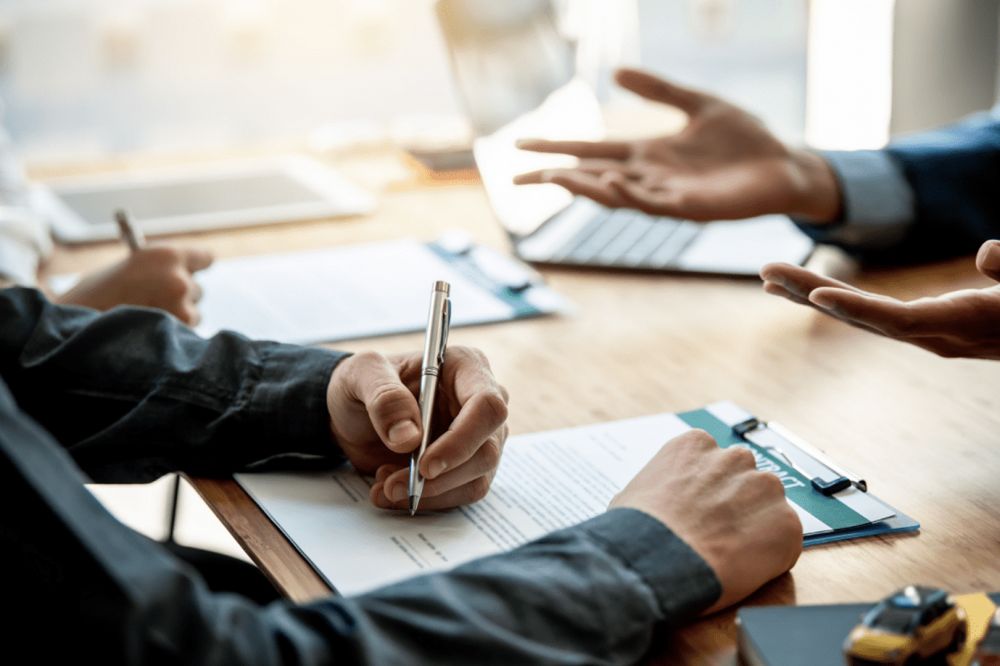 Business meeting with hands gesturing, documents on table, and person writing notes with a pen.
