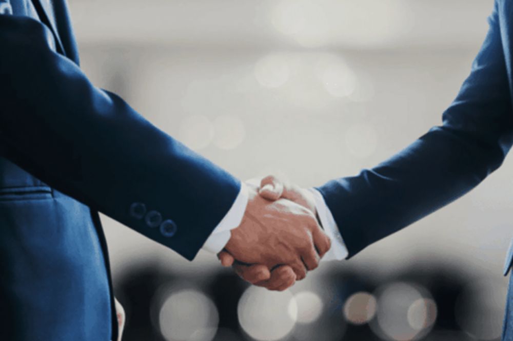 Business handshake between two people in suits against a blurred background.