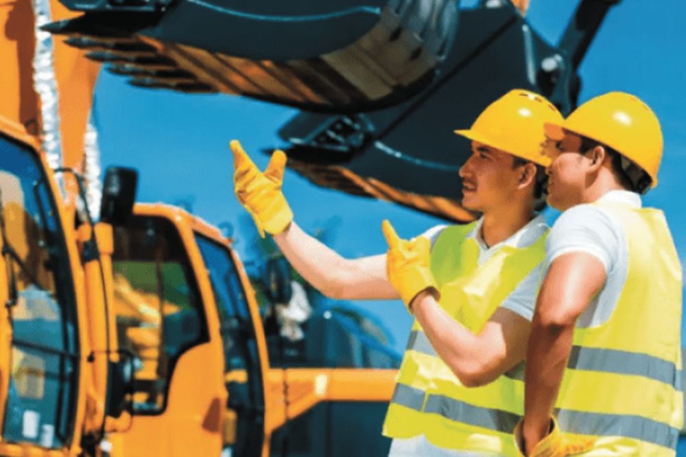 Construction workers in safety gear discussing operations at a site with heavy machinery in the background.