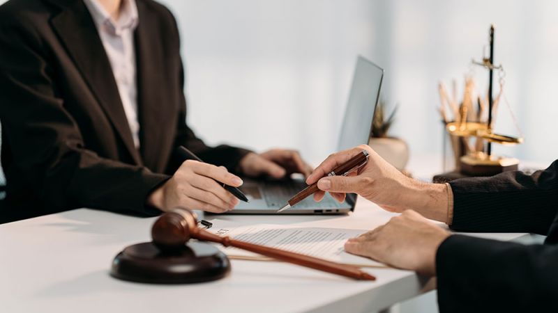 Lawyers discussing contract with gavel and scales in view, symbolizing legal advice, consultation, and justice.
