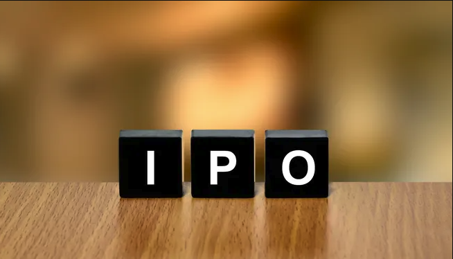 Three black letter tiles on a wooden table spell 'IPO' with a blurred warm background.