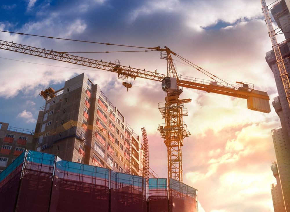 Construction site with cranes and building under sunset sky. Urban development and architecture.